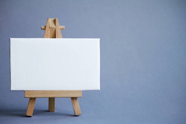 A miniature easel with a white board for writing, pointer on white surface, concept of direction and graphics, selective focus
