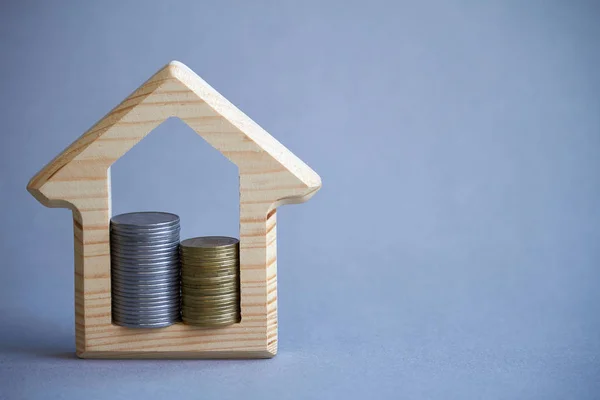 Trä figurin i huset och två kolumner av mynt inne på grå bakgrund, begreppet köpa eller hyra en byggnad, miljövänlig för miljön, selektiv fokus — Stockfoto