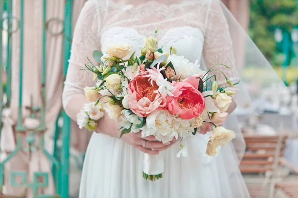 Die Braut hält einen Strauß frischer Frühlings- und Sommerblumen in Pastellfarben auf einem unscharfen Hintergrund, selektiver Fokus — Stockfoto