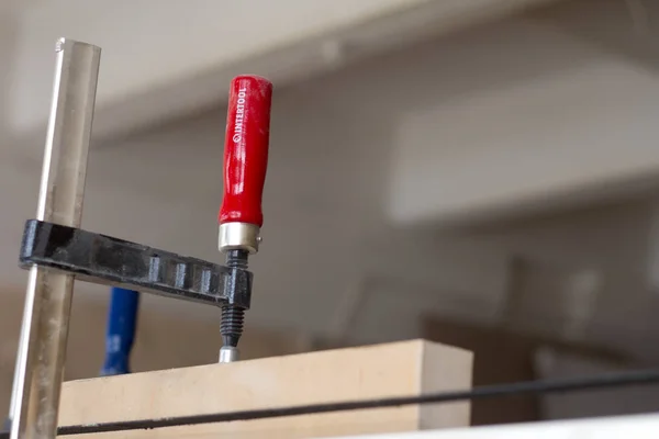 Pegado y fijación de muebles de madera con unas pinzas sobre un fondo borroso de un taller de carpintería, enfoque selectivo —  Fotos de Stock