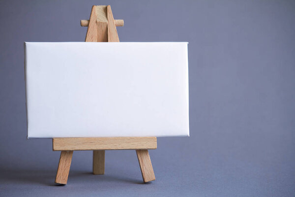 A miniature easel with a white board for writing, pointer on white surface, concept of direction and graphics, selective focus