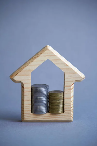 Figurinha de madeira da casa e duas colunas de moedas dentro em fundo cinza, o conceito de comprar ou alugar um edifício, eco-friendly para o meio ambiente, foco seletivo — Fotografia de Stock