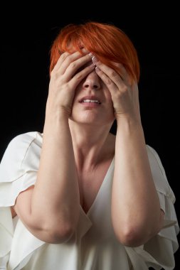 Yetişkin kızıl saçlı kadın şaşırdığı ya da korktuğu için eliyle gözlerini kapadı, siyah bir arka plan üzerine sürtündü, seçici odak