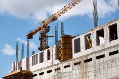 Yüksek katlı bir binanın inşası, çimento desteklerinin oluşturulması ve mavi gökyüzüne karşı vinç çalışması, seçici odak