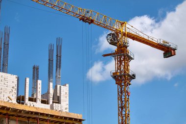 Yüksek katlı bir binanın inşası, çimento desteklerinin oluşturulması ve mavi gökyüzüne karşı vinç çalışması, seçici odak