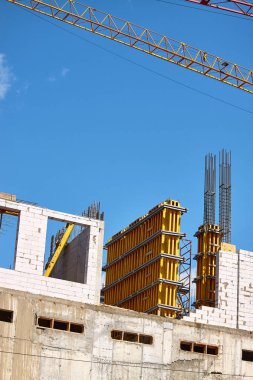 Yüksek katlı bir binanın inşası, çimento desteklerinin oluşturulması ve mavi gökyüzüne karşı vinç çalışması, seçici odak