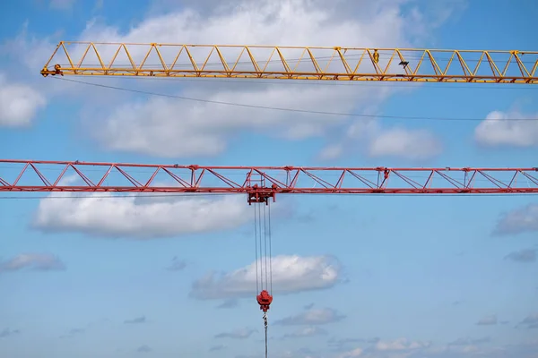 Close-up of two arrows of construction cranes arranged in parallel against a blue sky, selective focus