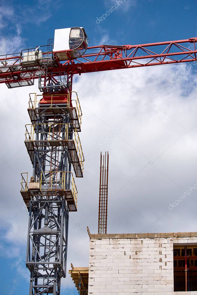 Close-up of the top of a blue tower crane near a new building against a blue sky, selective focus