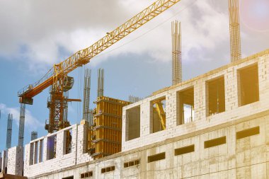 Yüksek katlı bir binanın inşası, çimento desteklerinin oluşturulması ve mavi gökyüzüne karşı vinç çalışması, seçici odak