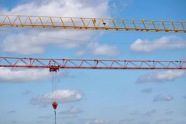 Close-up of two arrows of construction cranes arranged in parallel against a blue sky, selective focus