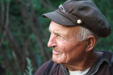 Close-up portrait of a very old man in a cap on a blurred background of green trees, selective focus clipart