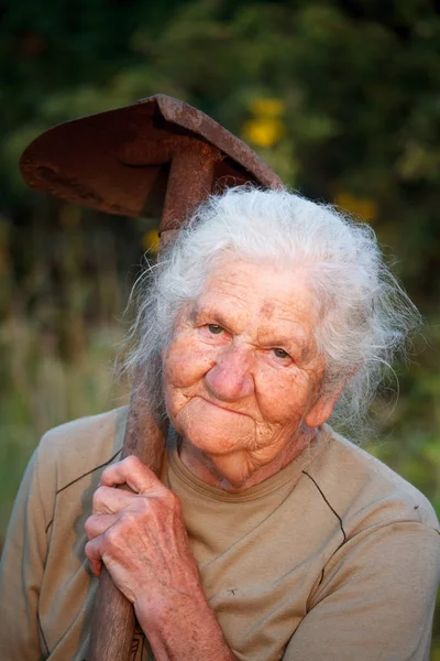 Nahaufnahme einer alten Frau mit grauen Haaren, die lächelnd in die Kamera blickt, mit einer rostigen Schaufel in den Händen, Gesicht in tiefen Falten, selektiver Fokus — Stockfoto