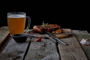 Büyük bir kızarmış biftek, bir bardak bira, hardal ve çatal bıçak takımı ile eski bir ahşap masa, Oktoberfest ve St Patrick Günü kavramı ile natürmort
