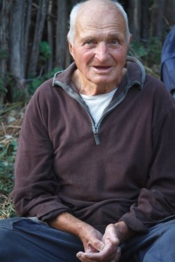 Kolları çapraz ile çok yaşlı bir adamın yakın çekim portre, ahşap çit bulanık bir arka plan üzerinde yere oturur, seçici odak