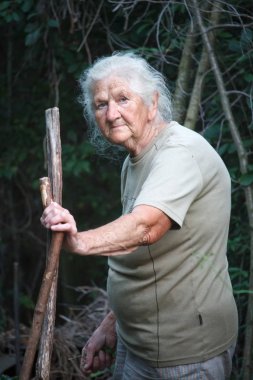 Portrait of an old woman with arthritic feet walking through the forest leaning on a stick as a cane, selective focus clipart