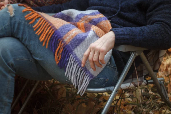 Close-up of an unrecognizable man in jeans and a sweater sitting on a folding deck chair in the autumn in the forest, a cozy autumn concept, selective focus — Stock Photo, Image