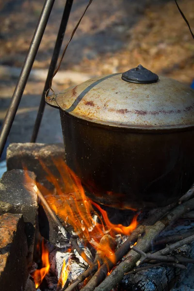 The concept of camping kitchen, on a tripod over a fire there is a pot in which food is prepared, selective focus