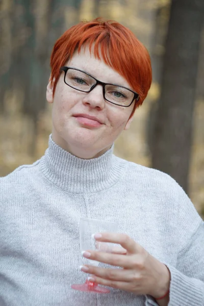 Retrato de cerca de una mujer pelirroja con gafas sobre un fondo borroso del bosque otoñal, enfoque selectivo — Foto de Stock