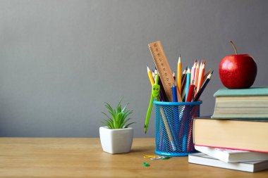 Geri okul kavramı, okul malzemeleri, kitap yığını, kırmızı elma ve ahşap bir yüzey üzerinde beyaz bir tencerede sulu, seçici odak