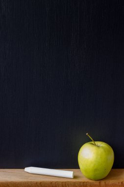 Okul konseptine geri dönelim, temiz siyah tebeşir tahtasının yakın çekimi, beyaz tebeşir ve yeşil elma, seçici odak, kopya alanı