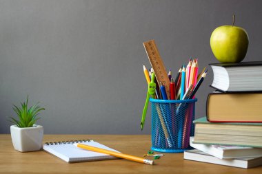 Okul konseptine, okul malzemelerine, kitap yığınına, yeşil elmaya, beyaz bir tencerede sulu ve ahşap bir yüzeye açık bir dizüstü bilgisayara, seçici odak