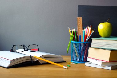 Geri okul kavramı, okul malzemeleri, kitap yığını, tebeşir tahtası ve ahşap bir yüzey üzerinde gözlük ile açık kitap, seçici odak