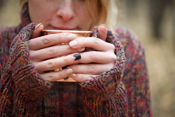 Close-up joven rubia en un suéter de punto caliente sosteniendo una taza de cobre con té o café, acogedor concepto de otoño, enfoque selectivo — Foto de Stock