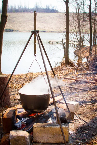 Kamp mutfak kavramı, bir yangın üzerinde bir tripod üzerinde gıda nehir ve köprüler, seçici odak arka planda hazırlanan bir tencere var — Stok fotoğraf