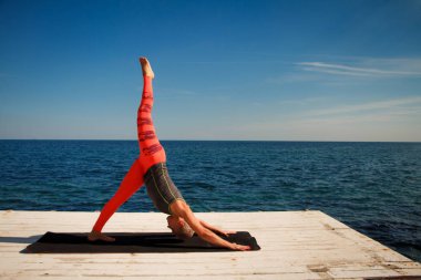 Kısa saç kesimi uygulamaları ile yetişkin sarışın kadın deniz ve mavi gökyüzü arka plan karşı iskelede yoga
