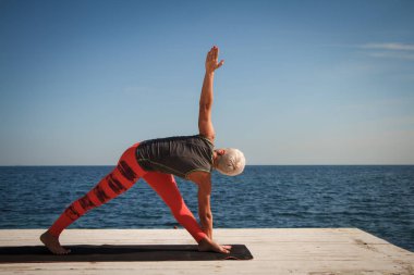 Kısa saç kesimi uygulamaları ile yetişkin sarışın kadın deniz ve mavi gökyüzü arka plan karşı iskelede yoga