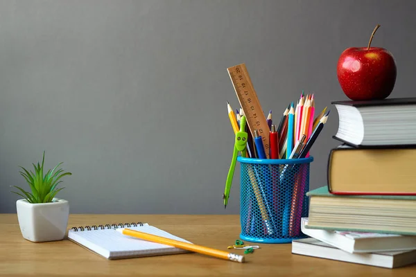 Okul konseptine, okul malzemelerine, kitap yığınına, kırmızı elmaya, beyaz bir tencerede sulu ve ahşap bir yüzeye açık bir deftere, seçici odak
