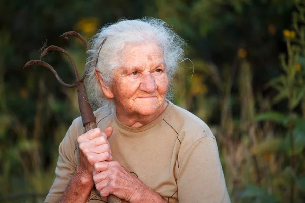 Close-up portret van een oude vrouw met grijs haar met een roestige Pitchfork of Chopper in haar handen, gezicht in diepe rimpels, selectieve focus — Stockfoto