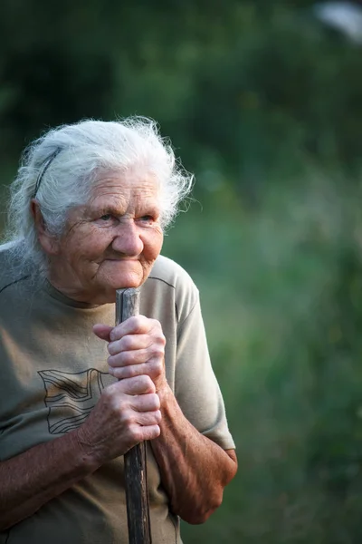 Ein Nahaufnahme-Porträt einer alten Frau mit grauen Haaren, die lächelt und nach oben blickt, ihr Kinn auf einem Stock ruht, als würde sie mit einem Stock gehen, Gesicht in tiefen Falten, selektiver Fokus — Stockfoto