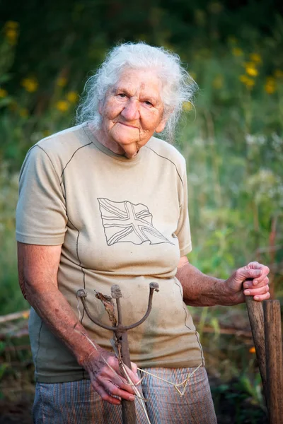 Retrato de una anciana con pies artríticos caminando en una pradera cubierta de hierba apoyada en un palo como un bastón, enfoque selectivo —  Fotos de Stock