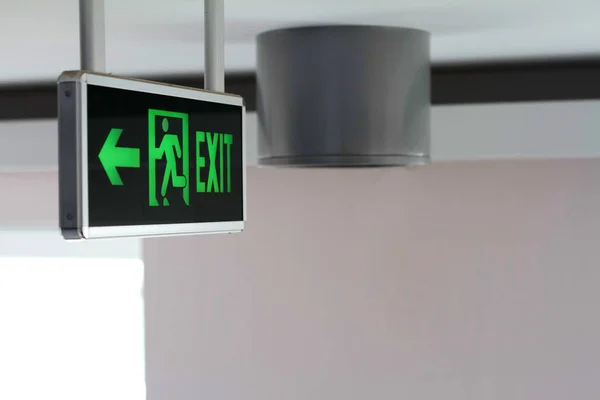Side view of a green glowing sign with the words Exit and a running man, selective focus