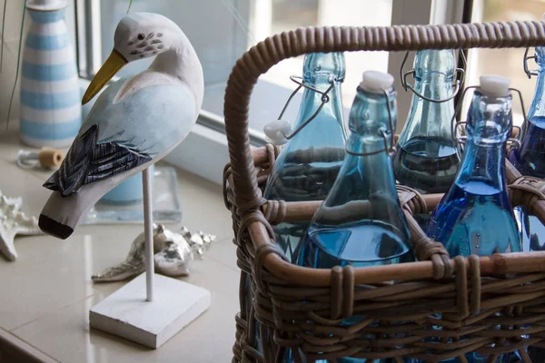 Крупним планом кілька скляних пляшок води в плетеному кошику і декоративний дерев'яний птах на підвіконні, вибірковий фокус — стокове фото