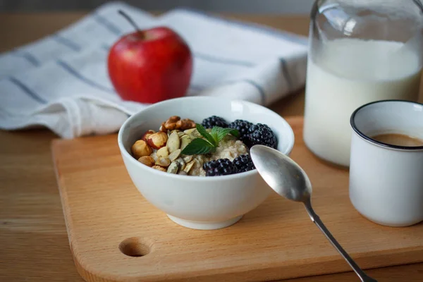 Top view oatmeal porridge, coffee, apple, berries, nuts and a bottle of milk on a wooden table, selective focus — Stock Photo, Image