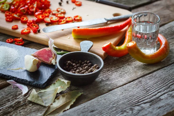 Närbild av en vinäger glas och hela peppar bredvid en bräda med hackad chilipeppar på en gammal träyta, selektiv fokus — Stockfoto