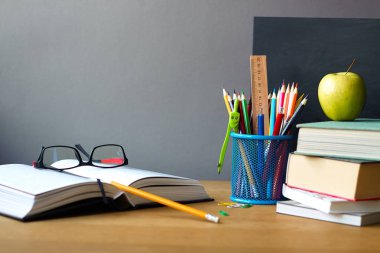Okul malzemeleri, kitap yığını, tebeşir tahtası ve ahşap bir yüzey üzerinde gözlük ile açık kitap, seçici odak