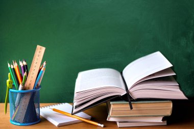 Okul malzemeleri, kitap yığını, tebeşir tahtası ve ahşap bir yüzey üzerinde açık kitap, seçici odak