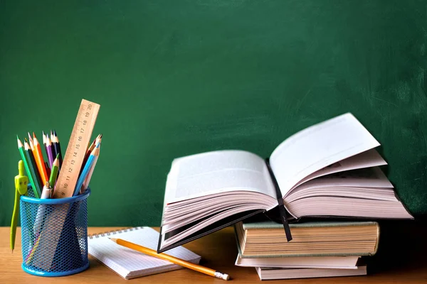 Okul malzemeleri, kitap yığını, tebeşir tahtası ve ahşap bir yüzey üzerinde açık kitap, seçici odak