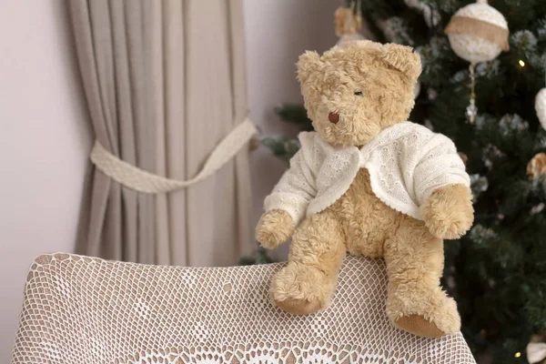 Juguete de primer plano Osito de peluche en la parte posterior de una silla con una envoltura de punto hecha a mano sobre un fondo borroso de un árbol de Navidad decorado, enfoque selectivo — Foto de Stock