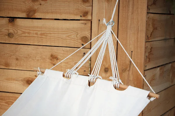 Close-up of a white hammock made of natural fabric on a wooden base hanging on ropes against a wooden wall, concept of natural relaxation — Stock Photo, Image