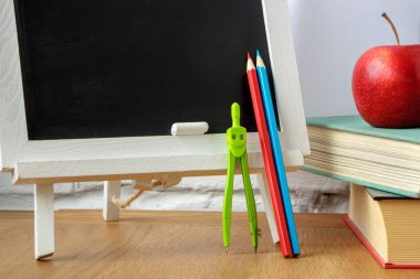 Okul malzemeleri, minyatür tebeşir tahtası, bir yığın kitap ve masada bir elma, yumuşak odak