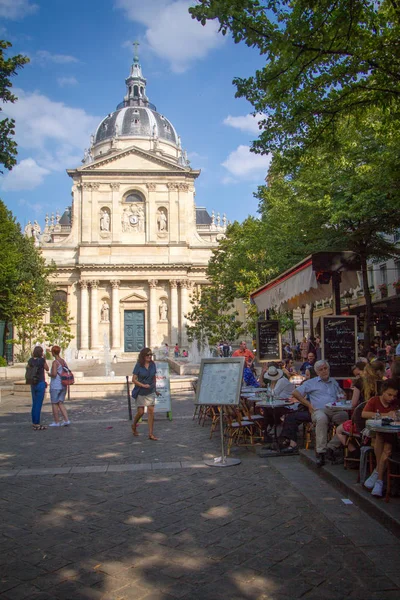 La gente se sienta en las mesas en la terraza de verano de la cafetería frente a la entrada principal de la Sorbona universitaria en París — Foto de Stock