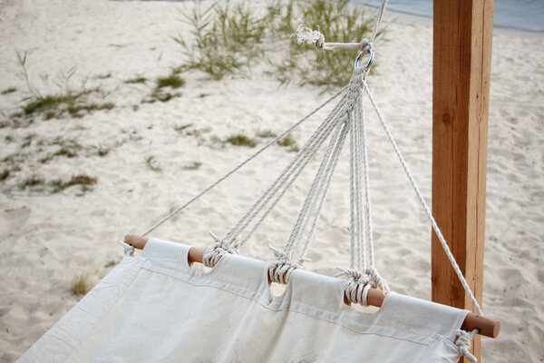 Close-up of a white hammock made of natural fabric on a wooden base hanging on ropes against a sandy beach, concept of natural relaxation Royalty Free Stock Images