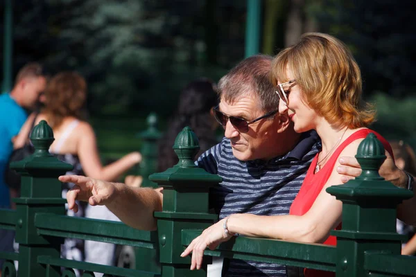 Μεσήλικα ζευγάρι χαμογελά και αγκαλιάζει σε μια βόλτα σε ένα δημόσιο πάρκο, στο φόντο του σιντριβάνι, επιλεκτική εστίαση — Φωτογραφία Αρχείου