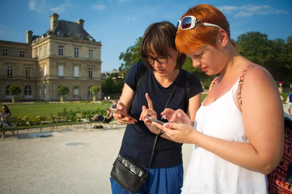 Two girls look at a smartphone at Luxembourg Palace, Jardin du Luxembourg is public park in Paris, garden of the French Senate. — Stock Photo, Image