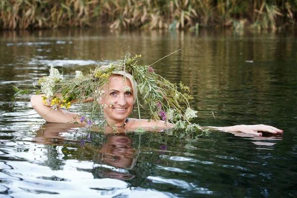 Close-up woman middle-aged blonde wreath of wildflowers on her head swims in the lake, selective focus Royalty Free Stock Photos