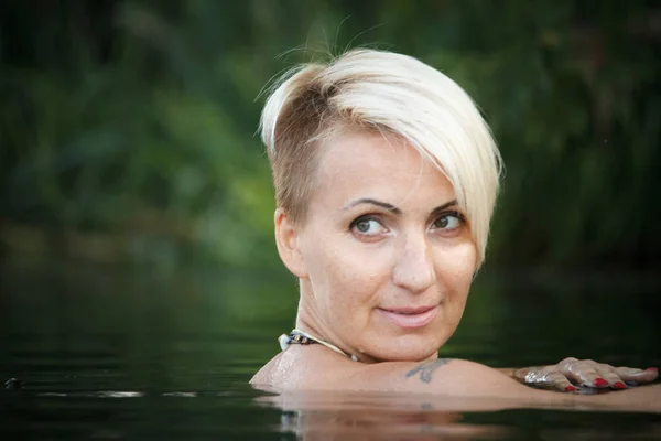 Close-up of a woman blonde middle-aged nude swims in the river, selective focus — Stock Photo, Image